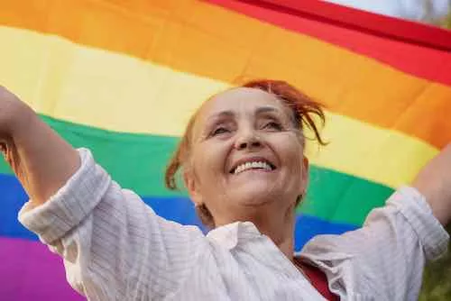 Beautiful mature senior woman with charming smile holding rainbow LGBT flag in her hands, gay and lesbian rights concept