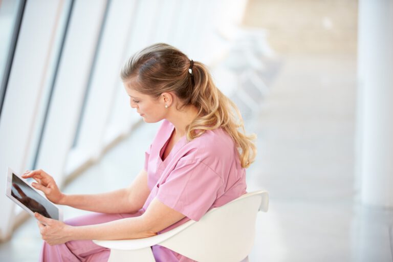 Female Nurse Sitting In Chair Using Digital Tablet